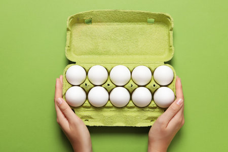 Female hands hold egg box on green background