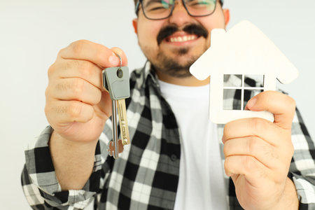 Concept of buying a house, happy young man with keys and house on light backgroundの写真素材