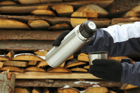 A woman pours a drink from a thermo  into the lid outdoorの写真素材