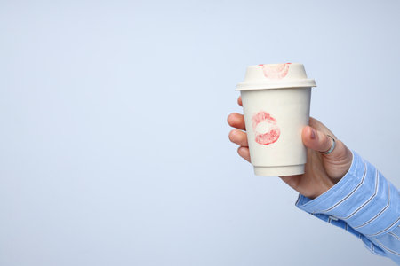 Female hand with paper cup with lipstick kisses on white backgroundの写真素材
