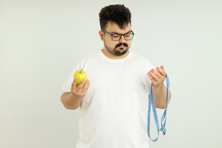 Concept of weight loss, fat guy with apple and measuring tape on white background