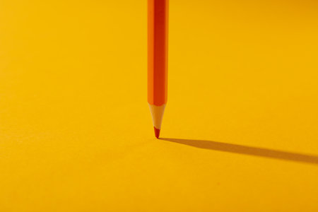 Orange pencil on yellow background, close upの写真素材