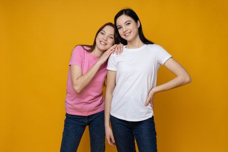 Two beautiful young women, sisters - twins on yellow backgroundの写真素材