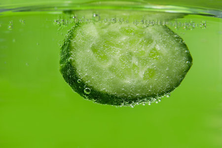 Slice of cucumber in water against green background