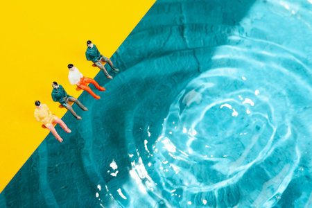Toy people sitting on yellow background near waterの写真素材