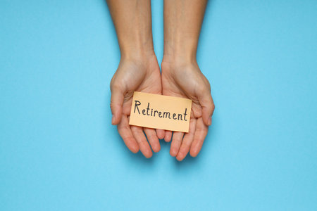 Female hands holding paper with text Retirement on blue backgroundの写真素材