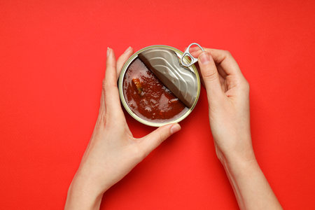 Canned fish in tomato and female hands on red backgroundの写真素材