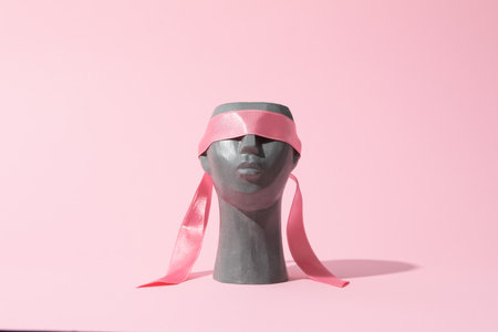 Decorative head with ribbon on eyes on pink backgroundの写真素材