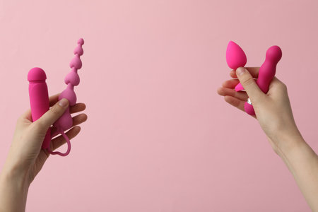 A collection of pink sex toys on a pink background in handsの写真素材