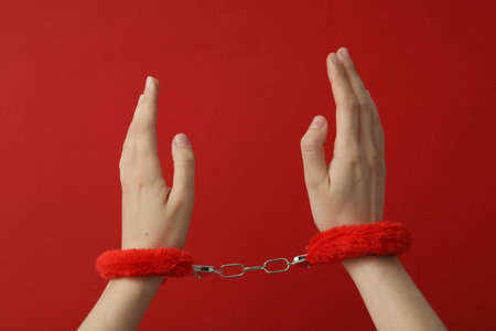 Red fluffy handcuffs on the hands on a red backgroundの写真素材