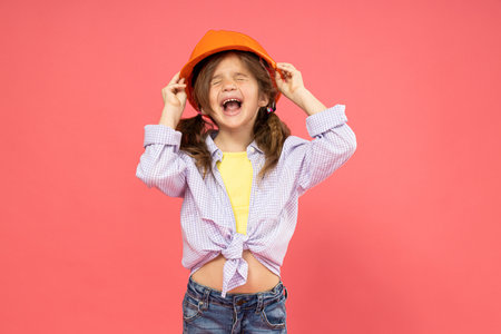 Little girl in construction helmet on pink backgroundの写真素材
