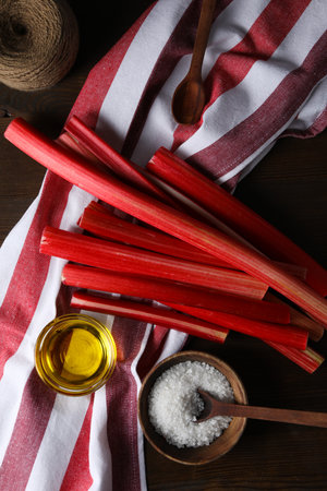 Rhubarb stalk on striped light towel, bowls and spoons on dark wooden backgroundの写真素材