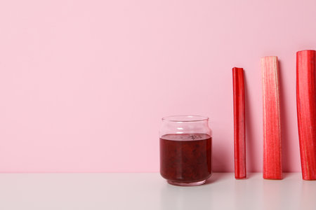 Jar of jam and stalks of rhubarb stand on light pink background, space for textの写真素材