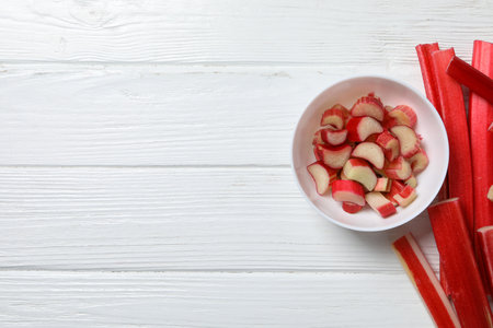 Rhubarb stalk and rhubarb pieces in bowl on white wooden background, space for textの写真素材