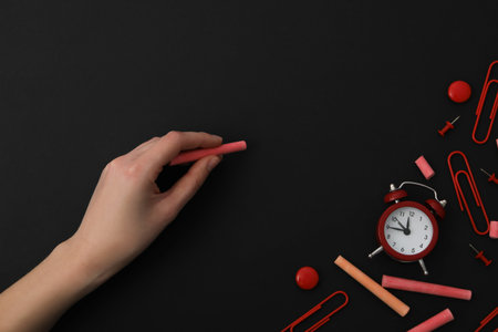 Piece of chalk in hand with clock on black background, place for textの写真素材
