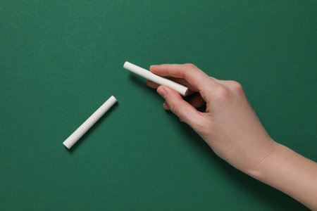 A piece of chalk in the hand on the background of a green school boardの写真素材