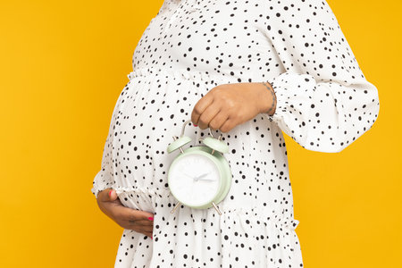 Pregnant woman on a yellow background with a clockの写真素材