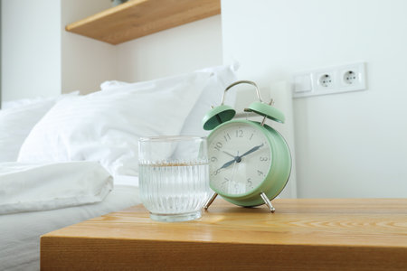 A green alarm clock and a glass of water on the bedside table