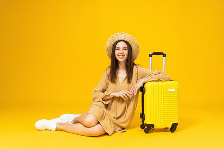 Young woman in a beach hat and a suitcase on a yellow backgroundの写真素材
