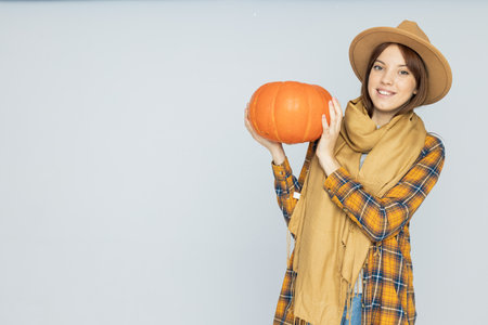 Attractive young woman in a hat with a pumpkin in her hands on a gray background, place for textの写真素材