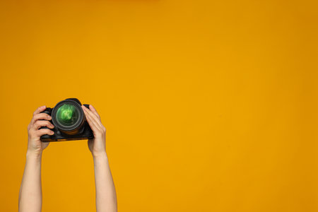 Camera in hands on yellow background with place for textの写真素材