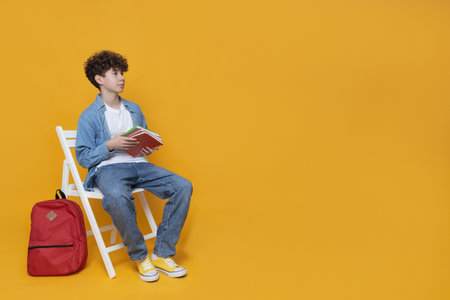 A teenager sits on a chair with a backpack and books, space for textの写真素材