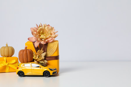 A toy car with a pumpkin, a flower and a gift on a light background, place for textの写真素材