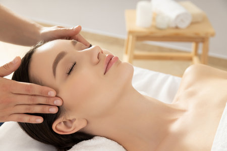 Young woman on face massage, masseur hands on light backgroundの写真素材