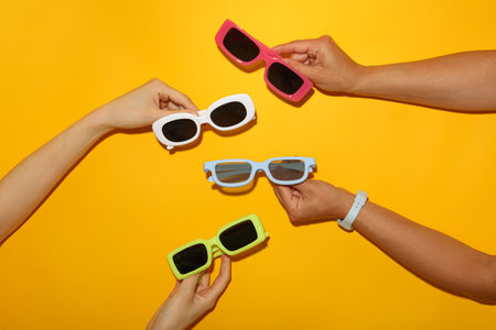 Colorful sunglasses in female hands on yellow background