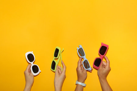 Colorful sunglasses in female hands on yellow background, space for textの写真素材
