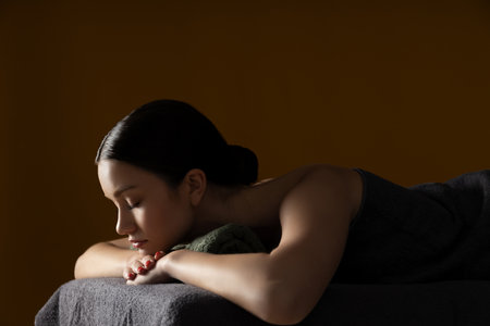 Brunette woman on massage table, brown background, space for textの写真素材