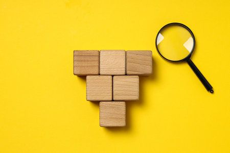 Lens and wooden cubes on yellow background, space for text