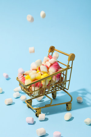Jelly candies and marshmallows in shopping trolley on blue backgroundの写真素材