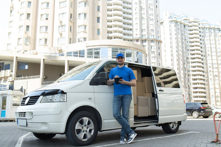 A courier with a tablet in his hands near a car with boxes