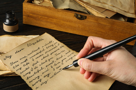 Old letter with text, pen in hand and ink bottle on wooden backgroundの写真素材