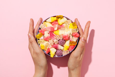 Jelly candies in box and female hands on pink background, top viewの写真素材