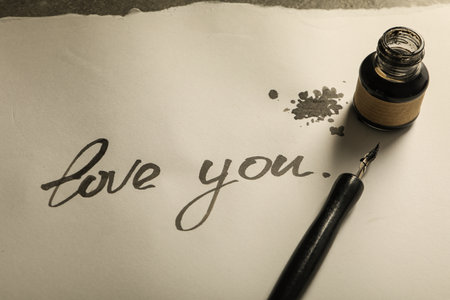 Ink bottle, pen and words Love you on paper on gray background, close upの写真素材
