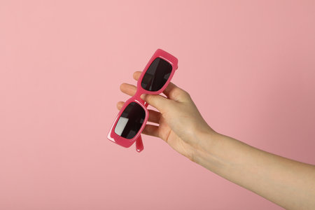 Pink sunglasses in female hand on pink backgroundの写真素材