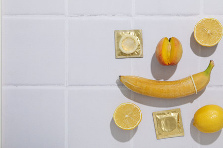 Condom on banana with peach and lemon on light background, place for textの写真素材