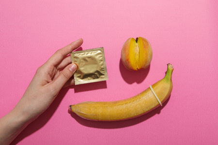 Condom on a banana with a peach on a pink backgroundの写真素材