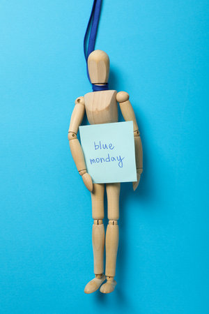 Wooden man on blue ribbon with paper with the text Blue Monday on blue background, top viewの写真素材
