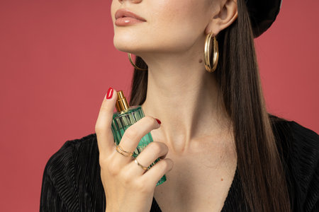 Young woman applying perfume on pink background