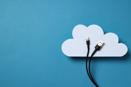 White, paper cloud with a black USB cable on a blue background, place for textの写真素材