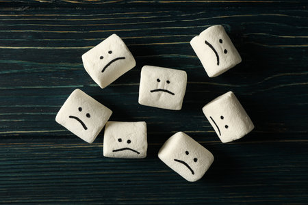 Marshmallow with sad emoji on dark blue wooden background, top viewの写真素材