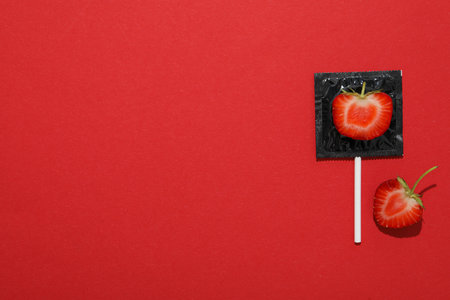 Black condom with strawberry on red background, place for textの写真素材