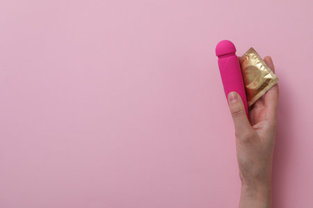 Condom and pink vibrator in hand on pink background, place for textの写真素材