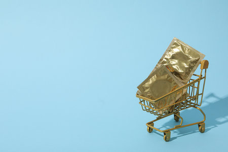 Condoms in shopping cart on blue background, place for textの写真素材