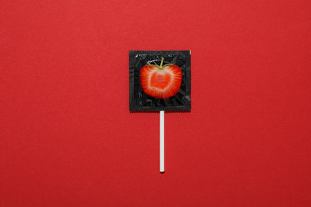 Black condom with strawberries on a red backgroundの写真素材
