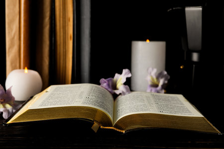 Open book, candles and flowers on dark background