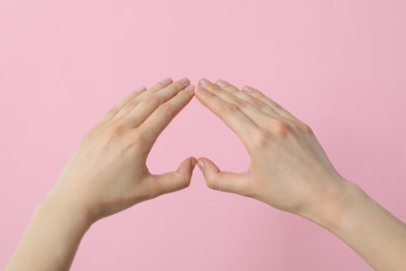 Female hands make a heart sign with fingers on a pink backgroundの写真素材